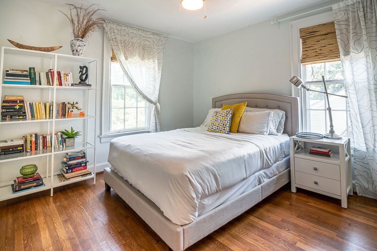 Bedroom with a full bookshelf, reading lamp and curtained windows