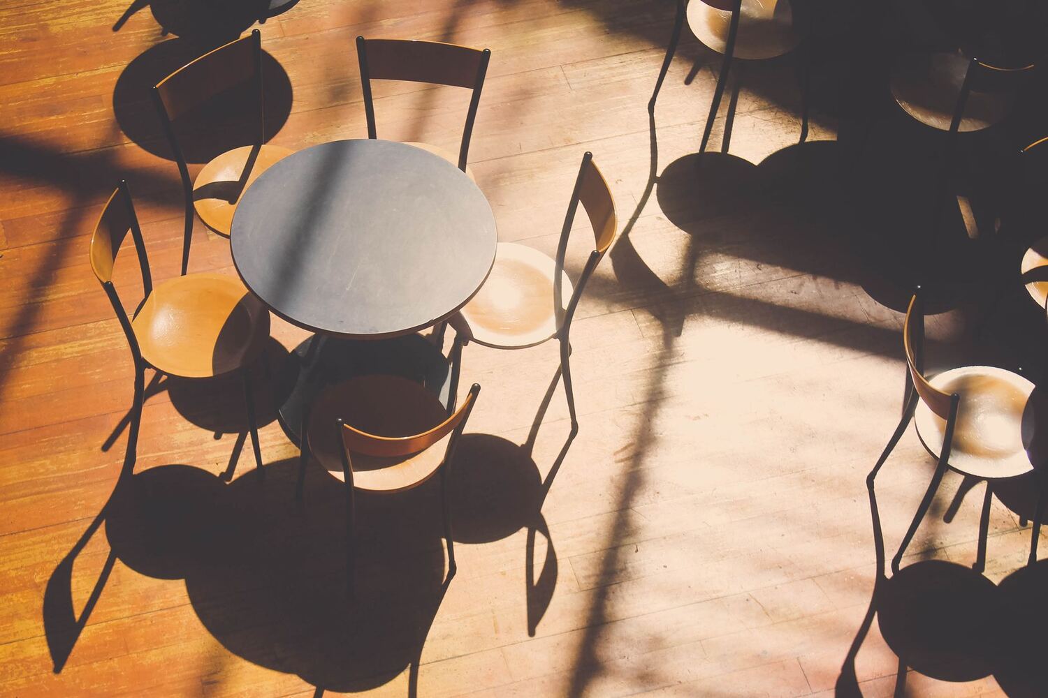 Empty cafe tables and chairs casting long shadows on a wood floor
