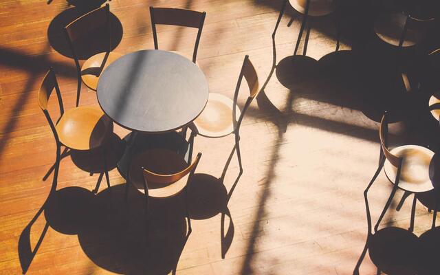 Empty cafe tables and chairs casting long shadows on a wood floor