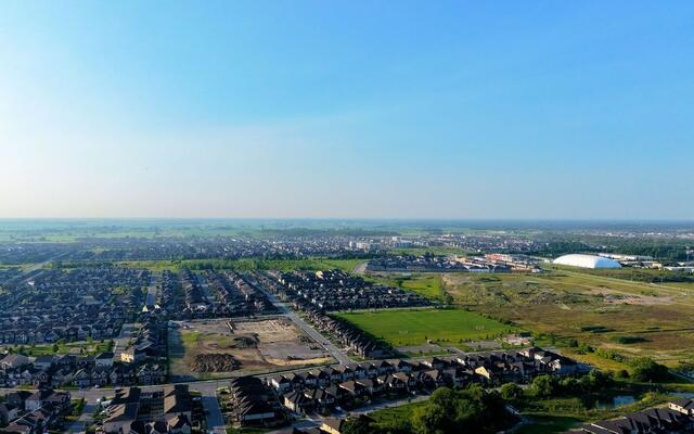 Aerial view of suburban rooftops meeting open fields under a wide sky