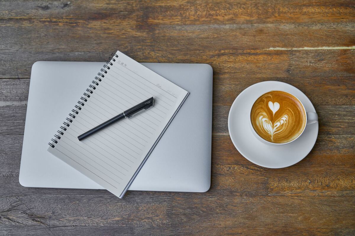 Laptop, ruled notebook and a latte on a wooden table