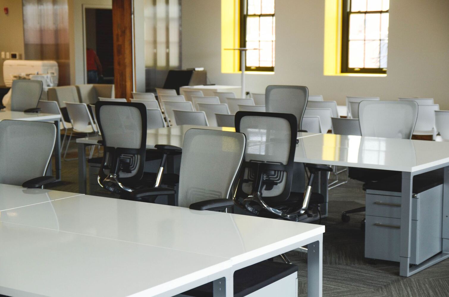 Open-plan office with rows of white desks and mesh chairs