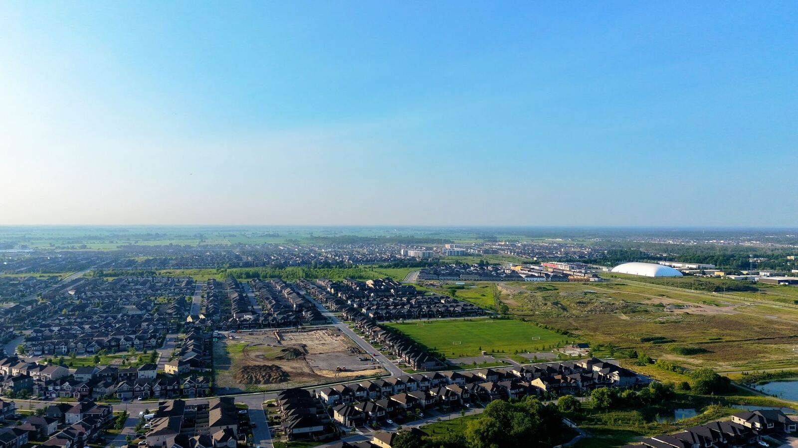 Aerial view of suburban rooftops meeting open fields under a wide sky