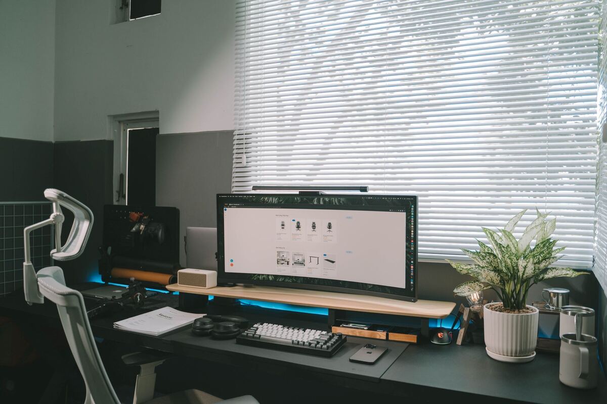 Wide monitor and keyboard on a desk in front of window blinds